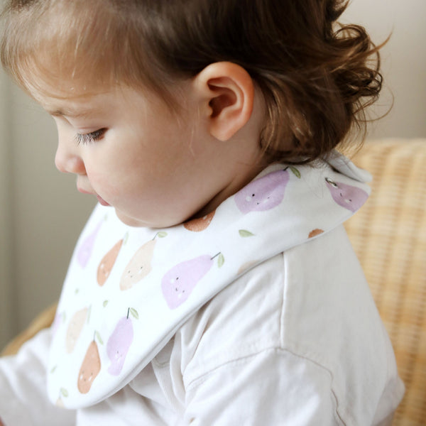 Child wearing a bib with pear patterns sitting on a wooden chair.