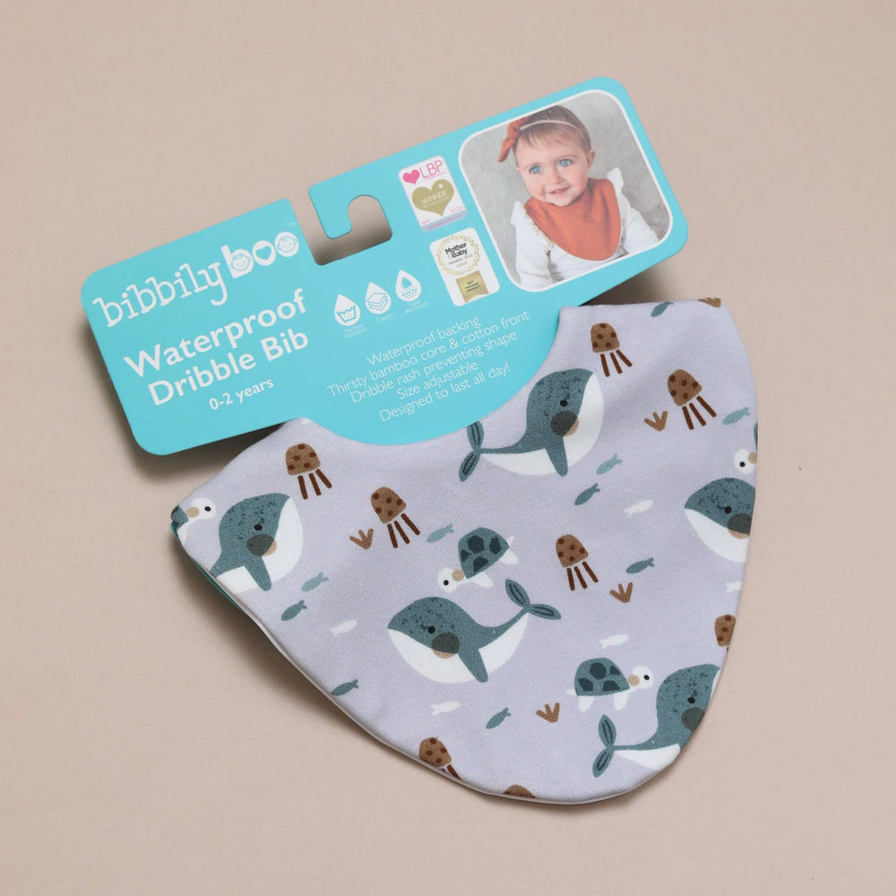 Baby bib with whale pattern and 'bibbilyboo' packaging on a beige background