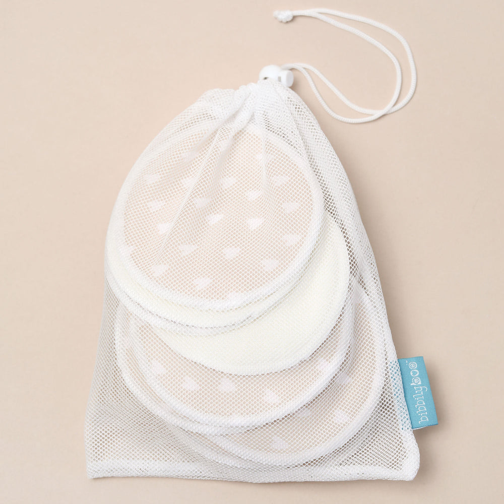 Set of white reusable breastfeeding pads with a laundry bag on a beige background