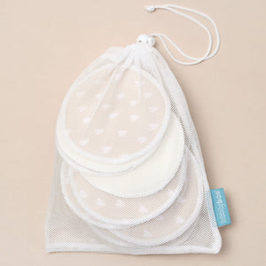 Set of bamboo and heart patterned breast pads in a mesh drawstring bag on a beige background