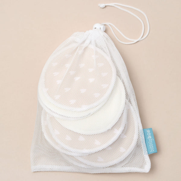 Set of bamboo and heart patterned breast pads in a mesh drawstring bag on a beige background