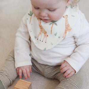Baby wearing a bib with giraffe design sitting on a couch.