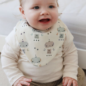 Baby sitting on a carpeted floor wearing a bib with robot design and striped pants.