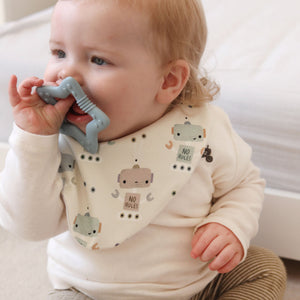Baby sitting on a carpeted floor wearing a bib with robot design, holding a gray teething toy.