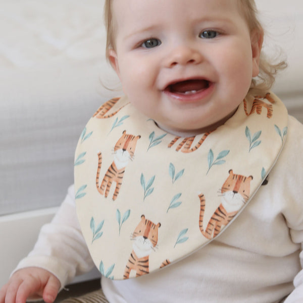 Baby wearing a bib with tiger design sitting on a couch.